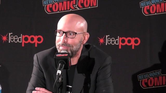 Brian K Vaughn wearing glasses in front of a Reedpop New York Comic Con background