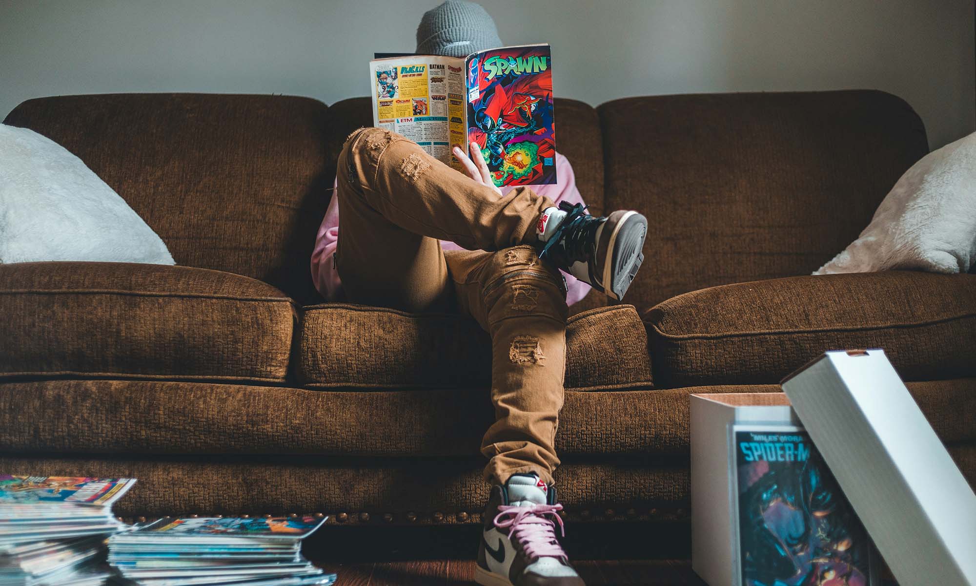Person in brown pants sitting on brown couch reading Spawn comics