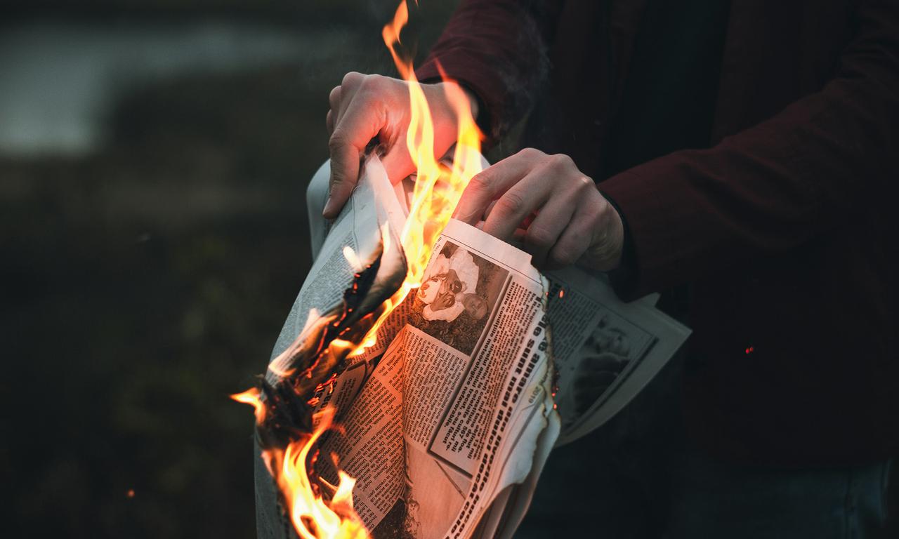 Person holding a burning newspaper