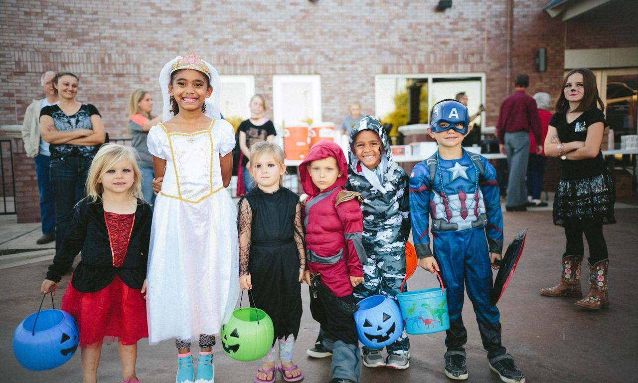 Children standing while holding jack o'latnerns and wearing costumes